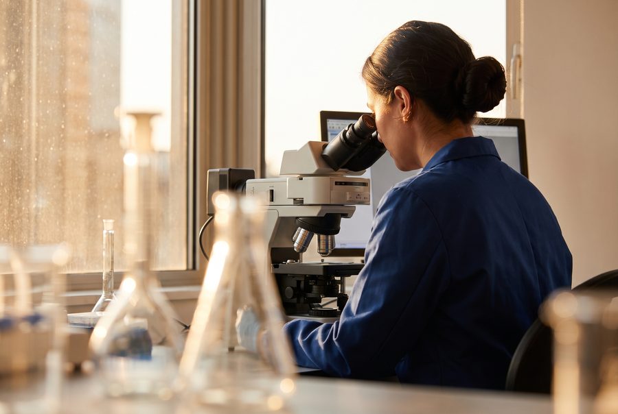 A scientist looking into a microscope in a sunlit laboratory